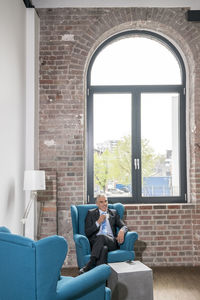 Mature businessman sitting in arm chair, drinking coffee