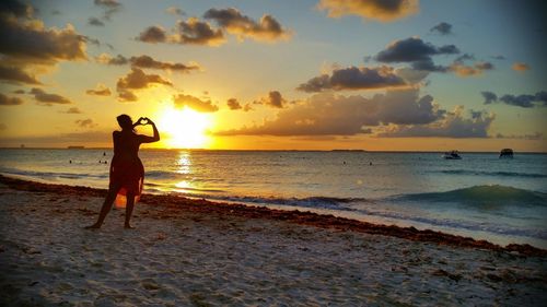 Silhouette woman standing on beach against sky during sunset