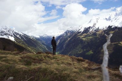 Rear view of man standing at mountains against cloudy sky