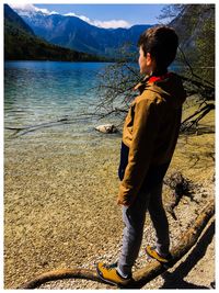 Boy standing on fallen tree against lake