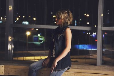 Woman sitting on window sill at night