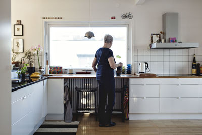 Full length rear view of senior woman standing in kitchen at home