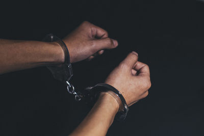 Cropped hands of man with handcuffs against black background