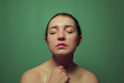Close-up of shirtless young woman with beauty product on face against green background