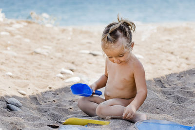 Naked girl playing with toys while sitting at beach
