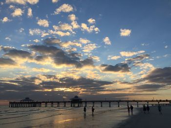 Silhouette people on beach against sky during sunset