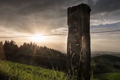 Wooden post on field against sky during sunset