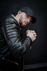 Portrait of man wearing cap and jacket against black background