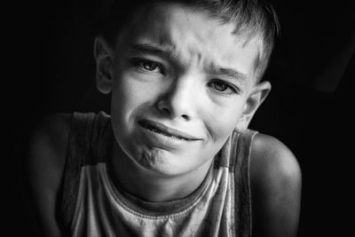 Close-up portrait of boy making face against black background