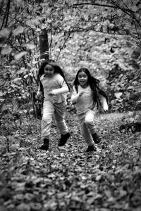 Full length of siblings running on field against trees at forest