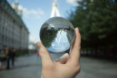 Close-up of hand holding crystal ball against trees