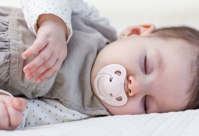 Close-up of baby with pacifier lying on bed