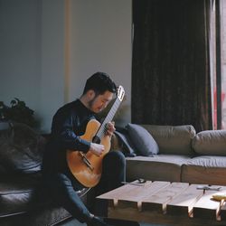 Young man playing guitar on sofa at home