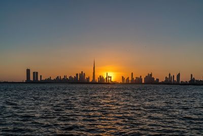 Sea and buildings against sky during sunset