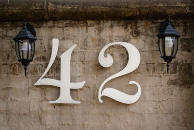 Close up of white metal street number 42 mounted against cement wall with black lamp on either side