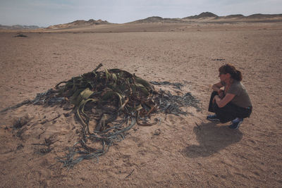 Woman with umbrella sitting on sand in desert