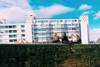 People on wall in city against sky