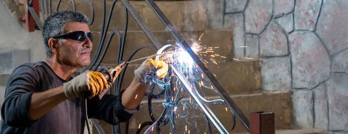 Man wearing protective glasses welds metal with welding machine in private house. sparks welding fly