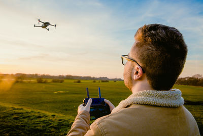 Man operating drone with remote control while standing on field 