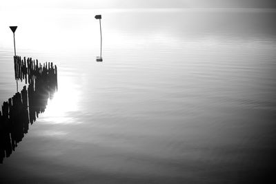 Silhouette of wooden posts in sea against sky