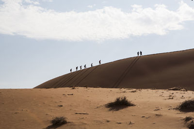 Mid distance view of hikers walking on sand dune at desert against sky