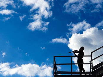 Low angle view of man standing on roof against sky