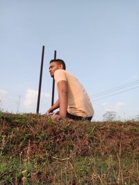 Low section of man sitting on field against sky