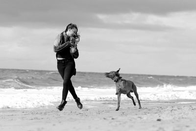 Full length of woman with dog running on shore at beach