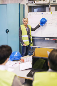 Mature female worker discussing plan on whiteboard to colleagues in factory