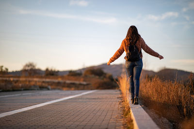 Rear view of woman walking on footpath against sky