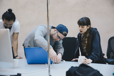 Computer programmer connecting cable laptop while colleagues at desk in office