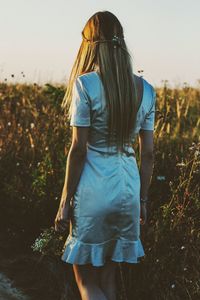 Rear view of young woman walking by plants on field