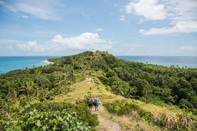 High angle view of people hiking on green mountain by sea