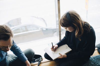 High angle view of businesswoman drawing on notepad while sitting by colleague in office cafeteria