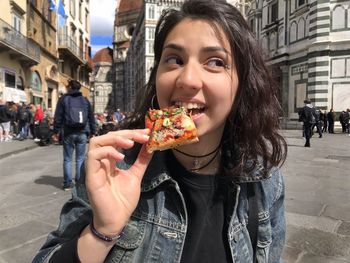 Young woman eating food on street in city
