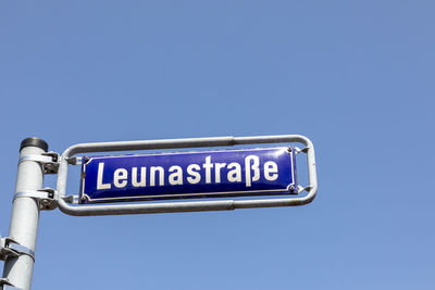 Low angle view of road sign against clear blue sky