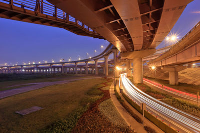 High angle view of light trails on roads below bridge at dusk