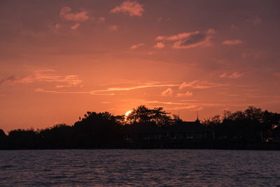 Silhouette trees by lake against romantic sky at sunset