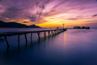 Silhouette pier over sea against cloudy sky during sunset