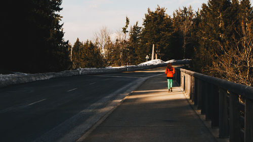 Rear view of woman walking on footpath by empty road