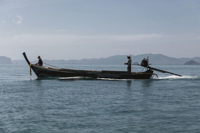 Men sailing boat in sea against sky