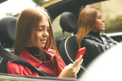 Girls sitting in the car. smiling teen in front of the steering wheel young women using smartphone