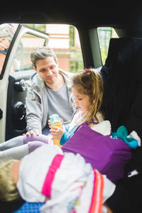 Father talking to sad girl sitting in car