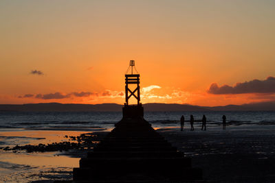 Silhouette lifeguard hut on beach against sky during sunset