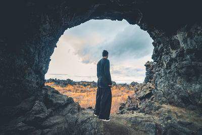 Rear view of man standing on rock against sky