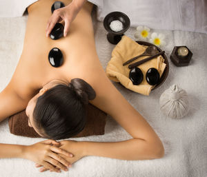 Cropped hand putting stones on woman back at spa