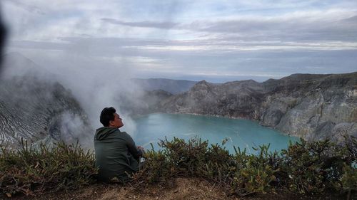 Rear view of man sitting on mountain against sky