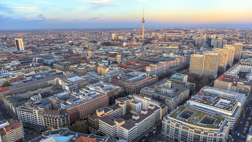 Fernsehturm amidst cityscape against sky during sunset