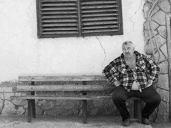 Full length portrait of overweight man sitting on bench against house