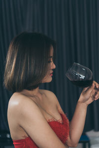 Close-up of woman drinking red wine against curtain